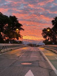 Road by trees against sky during sunset