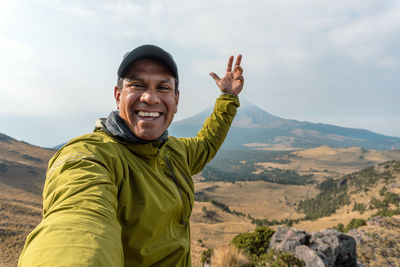 Portrait of young man standing on mountain against sky