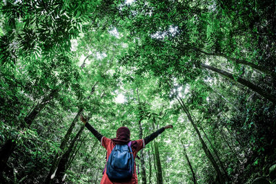 Low angle view of young woman with arms outstretched standing in forest