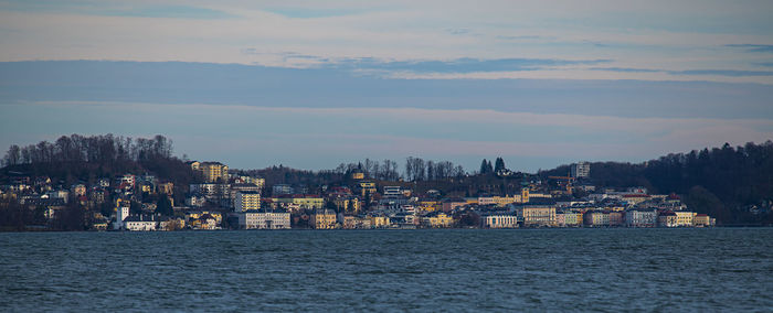 Illuminated buildings by sea against sky at sunset