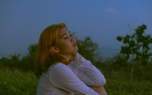 Portrait of woman looking away on field against sky