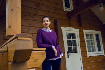 Young woman in a purple sweater and black jeans out on the porch of a wooden house