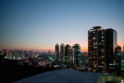 Illuminated buildings in city against clear sky at night