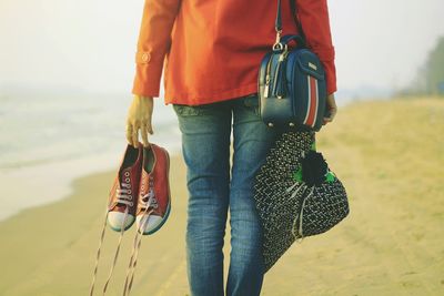 Low section of woman holding umbrella standing on beach