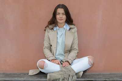 Portrait of young woman sitting against wall