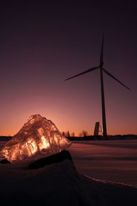 Windmill on snowcapped mountain against sky during sunset