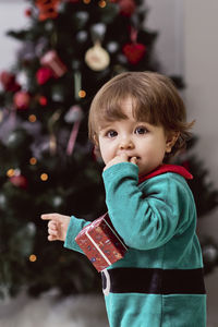 A little 12-month-old christmas elf with a christmas tree and gifts