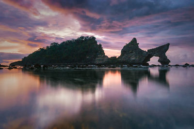 Reflection of rocks in sea against sky during sunset