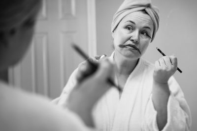 Mature woman applying make-up reflecting on mirror at home