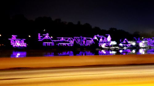 Illuminated text on road against sky at night