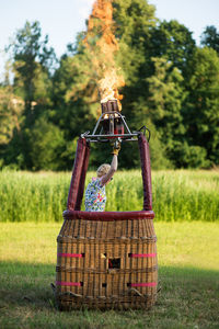 Female pilot preparing hot air balloon on grassy field against sky during sunset