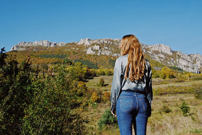 Rear view of woman walking on mountain against clear sky