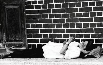 Senior man sleeping on footpath against brick wall