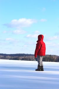 Boy in red jacket standing on snowy road against sky
