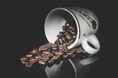 Close-up of roasted coffee beans falling on cup on glass table