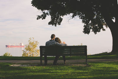 Rear view of couple sitting on bench against sky