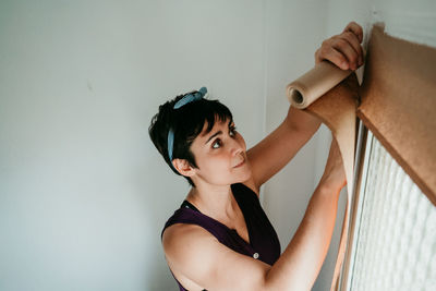 Portrait of young woman looking away while standing against wall at home