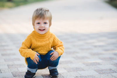 Happy child girl 3-4 year old wearing yellow knitted sweater playing in park outdoors. autumn season