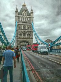 People walking on bridge against cloudy sky