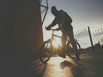 Full length of man with bicycle walking on street against sky during sunset