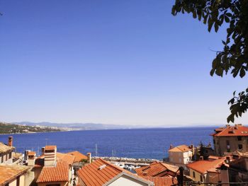 Buildings by sea against clear blue sky