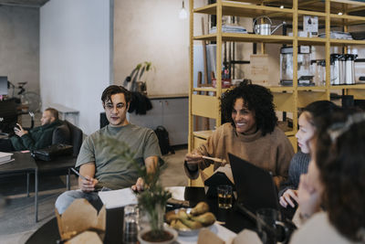 Smiling business colleagues discussing while having lunch at table in creative office