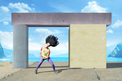 Portrait of smiling woman dancing against built structure and sea