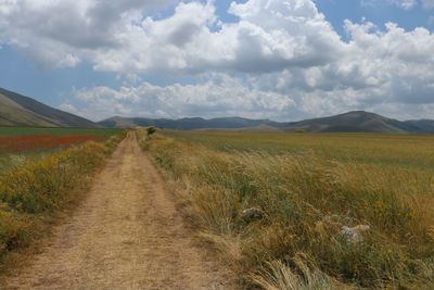 Dirt road amidst field against sky