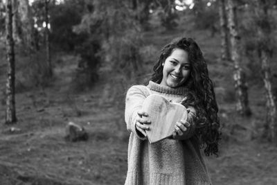 Portrait of smiling young woman holding heart shape in forest