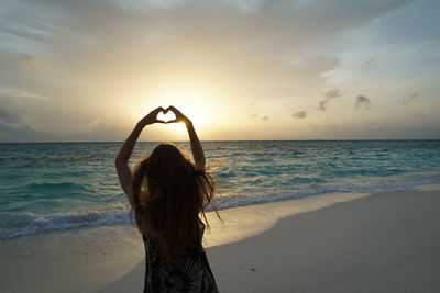 Rear view of woman standing at beach against sky during sunset