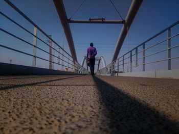 Surface level shot of man walking on bridge against clear sky