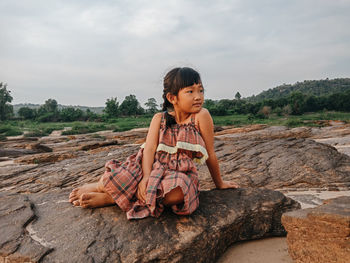 Girl sitting on rock against sky