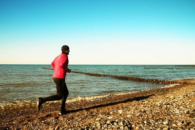 Tall man in dark sportswer running and exercising on stony beach at breakwater. vivid effect