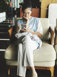 Young woman using mobile phone while sitting on sofa at home