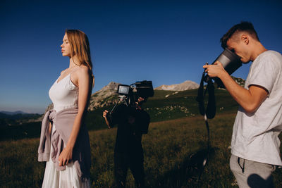 Young woman photographing on field against clear blue sky