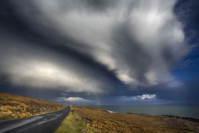 Road passing through landscape against cloudy sky