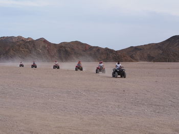 People riding quadbikes at desert against rocky mountains