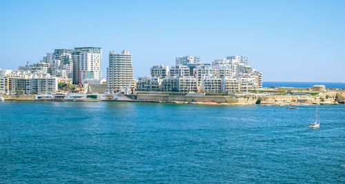 View of buildings in city at seaside against clear blue sky