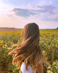 Rear view of woman on sunflower field against sky
