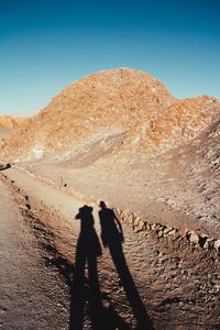 Shadow of two people on desert against clear sky