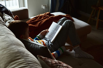 Child boy reading book on the sofa at home