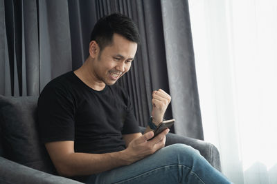 Cheerful man using mobile phone while sitting on sofa at home