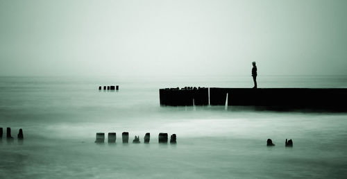 Silhouette person on pier at sea