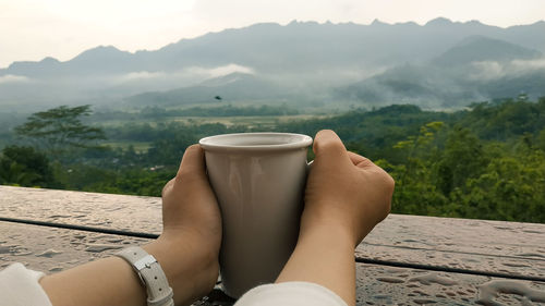 Midsection of woman holding coffee cup against mountains