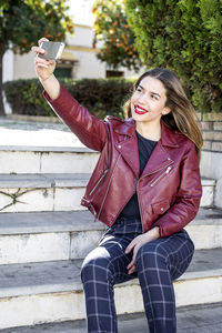 Cheerful young woman taking selfie while sitting on steps