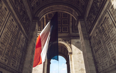 Low angle view of french flag by arc de triomphe in city