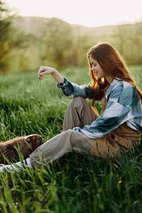 Side view of woman using mobile phone while sitting on field