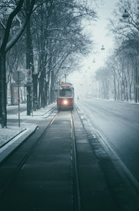 A retro tram with its headlights on during a snowfall moves towards