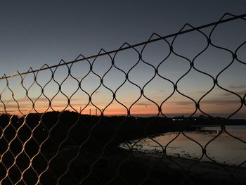 Silhouette chainlink fence against clear sky during sunset