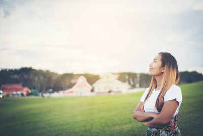 Smiling woman looking away while standing on field against sky